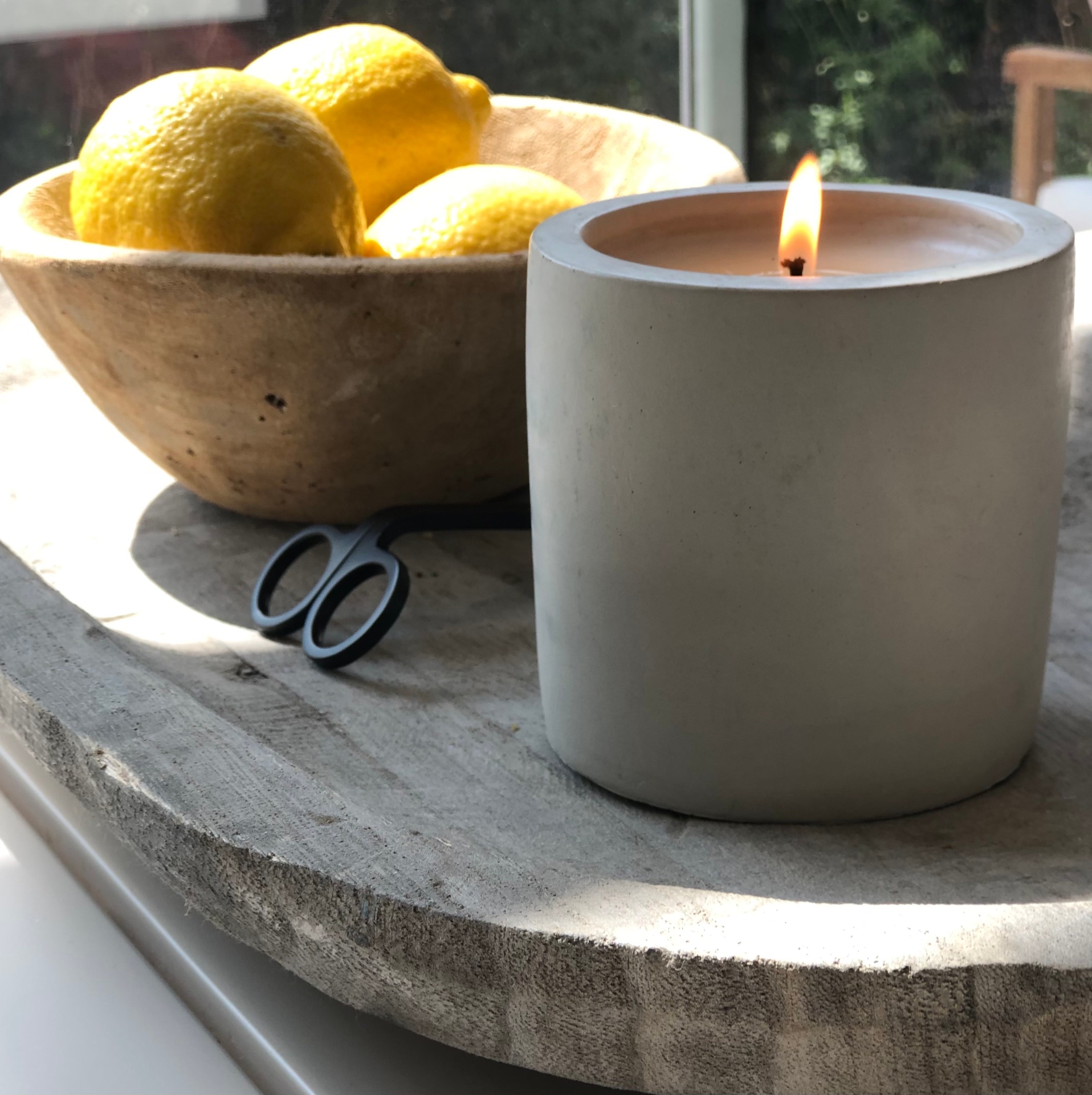 a lit candle beside lemons in warm window light, suggesting natural scent
